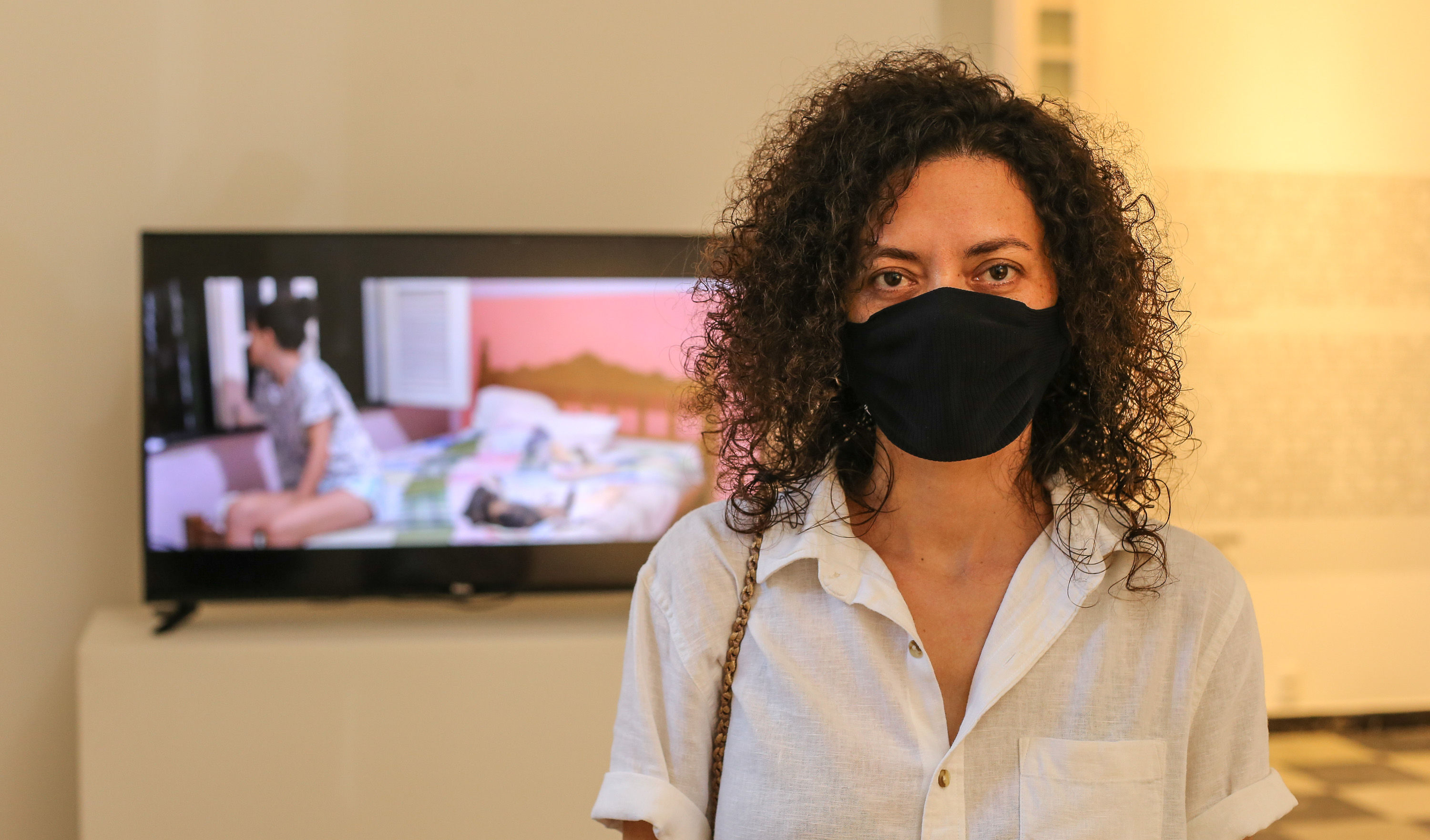 A artista plástica Nataly Rocha na frente de uma tela de TV que mostra sua videoarte